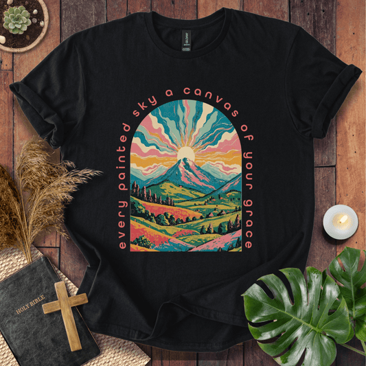“Every painted sky a canvas of Your grace” Christian t-shirt—arched mountain sunrise with rays, rolling hills, floral accents.