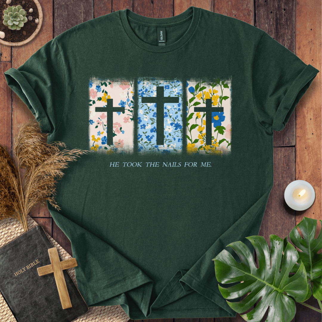 Christian Easter t-shirt with three floral crosses and "He Took The Nails For Me" text, styled on a rustic wood background.