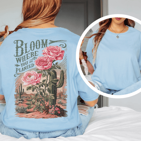 Back of a t-shirt featuring pink roses, green saguaro cacti, and text reading Bloom Where You Are Planted.
