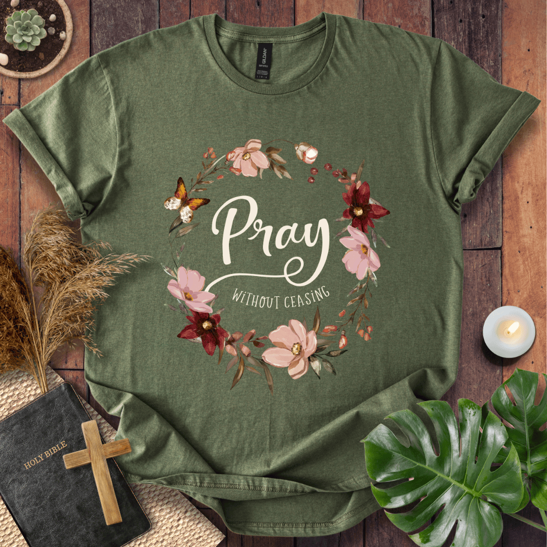"Pray Without Ceasing" text inside a floral wreath with a butterfly on a shirt next to a Bible and cross.