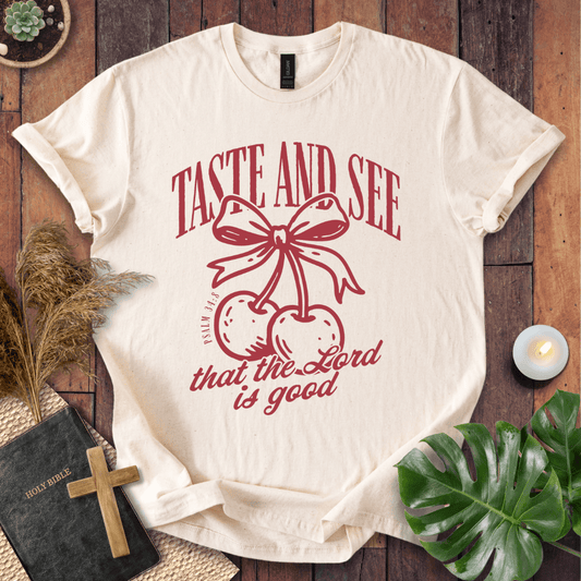White t-shirt with religious design and text on a wooden surface with decor items.