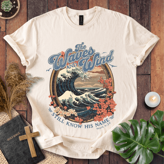The Waves and Wind Still Know His Name Christian t-shirt in sand—vintage wave, sunset, and floral frame, Mark 4:39.