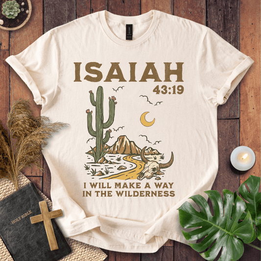 Beige t-shirt with cactus and skull design and 'ISAIAH 43:19' text on a wooden surface.