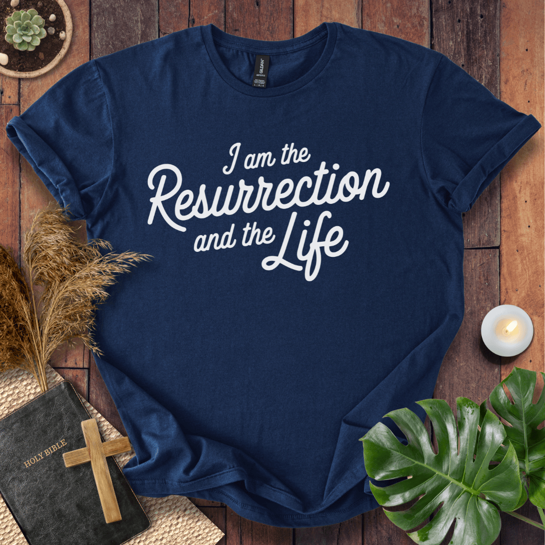 Christian t shirt for women featuring white script 'I am the Resurrection and the Life' on a rustic wood table.