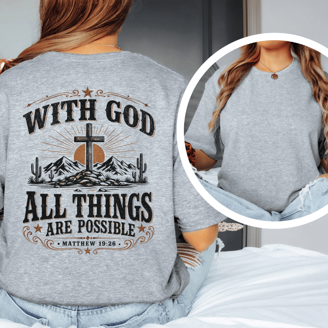 A woman sitting on a bed wearing a western faith shirt featuring a desert cross design and Matthew 19:26 scripture.