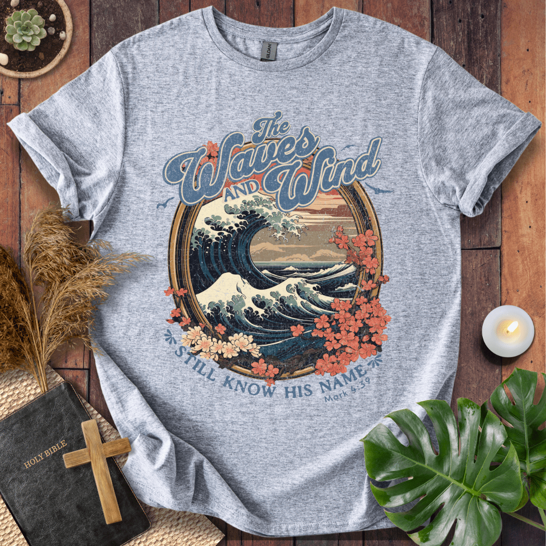 The Waves and Wind Still Know His Name Christian t-shirt in sand—vintage wave, sunset, and floral frame, Mark 4:39.