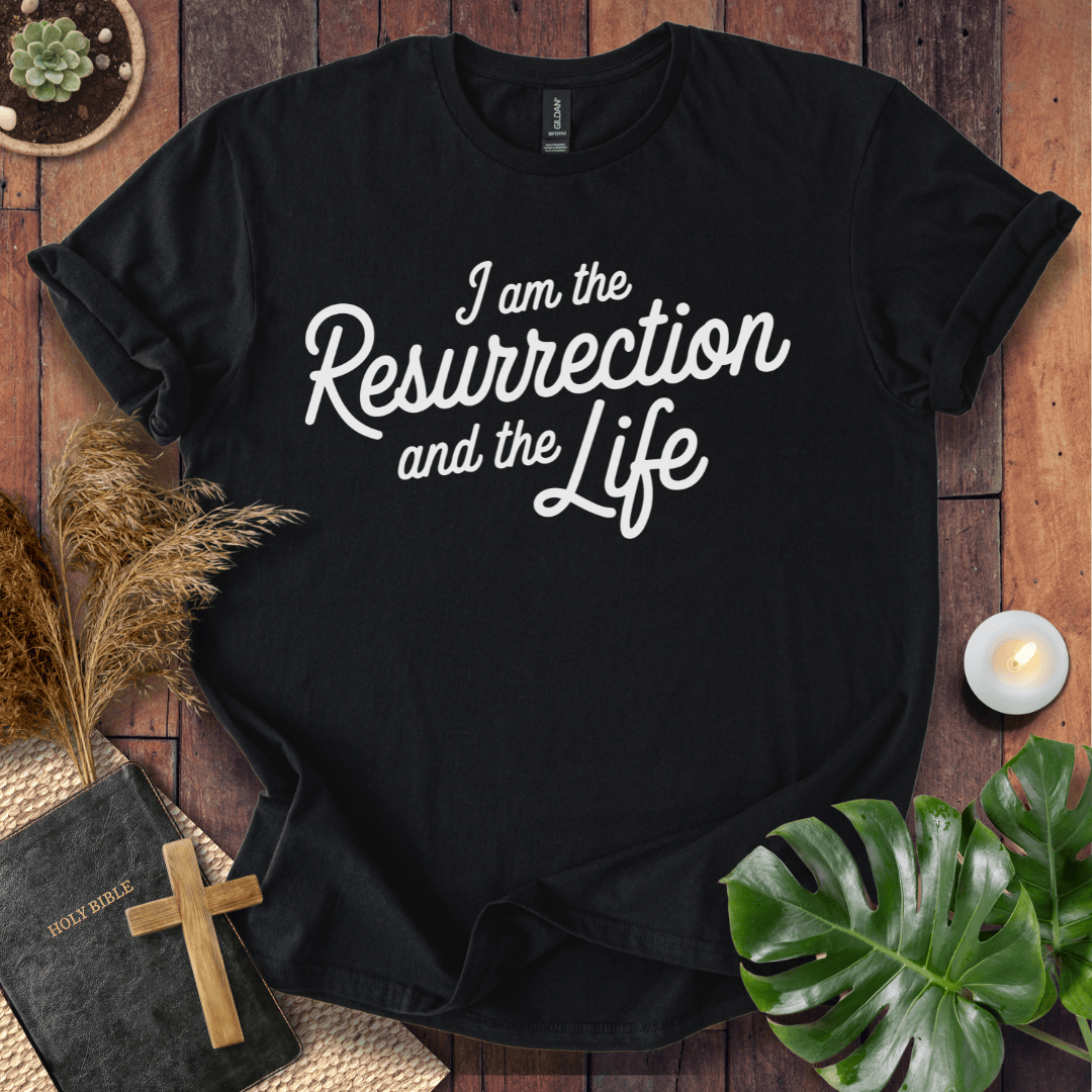 Christian t shirt for women featuring white script 'I am the Resurrection and the Life' on a rustic wood table.