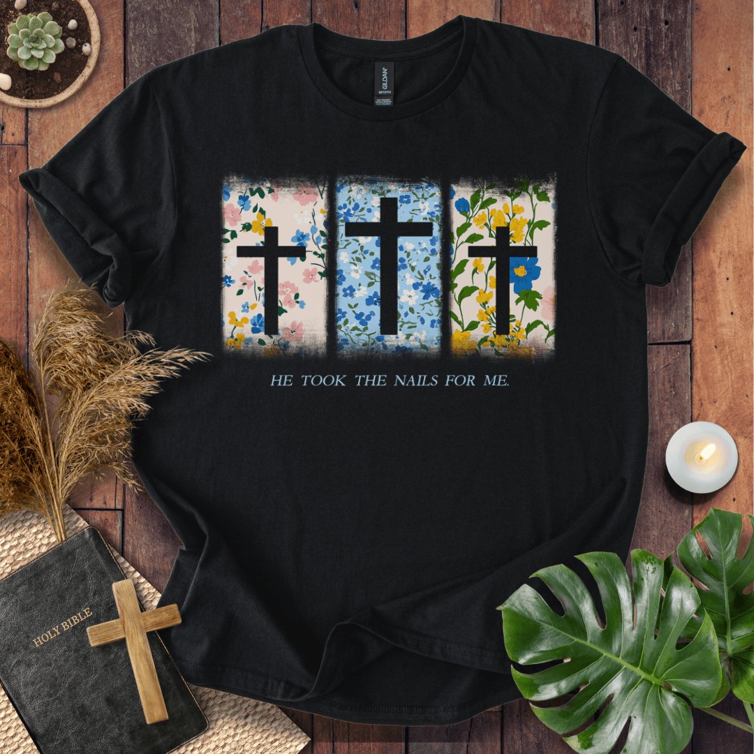 Christian Easter t-shirt with three floral crosses and "He Took The Nails For Me" text, styled on a rustic wood background.