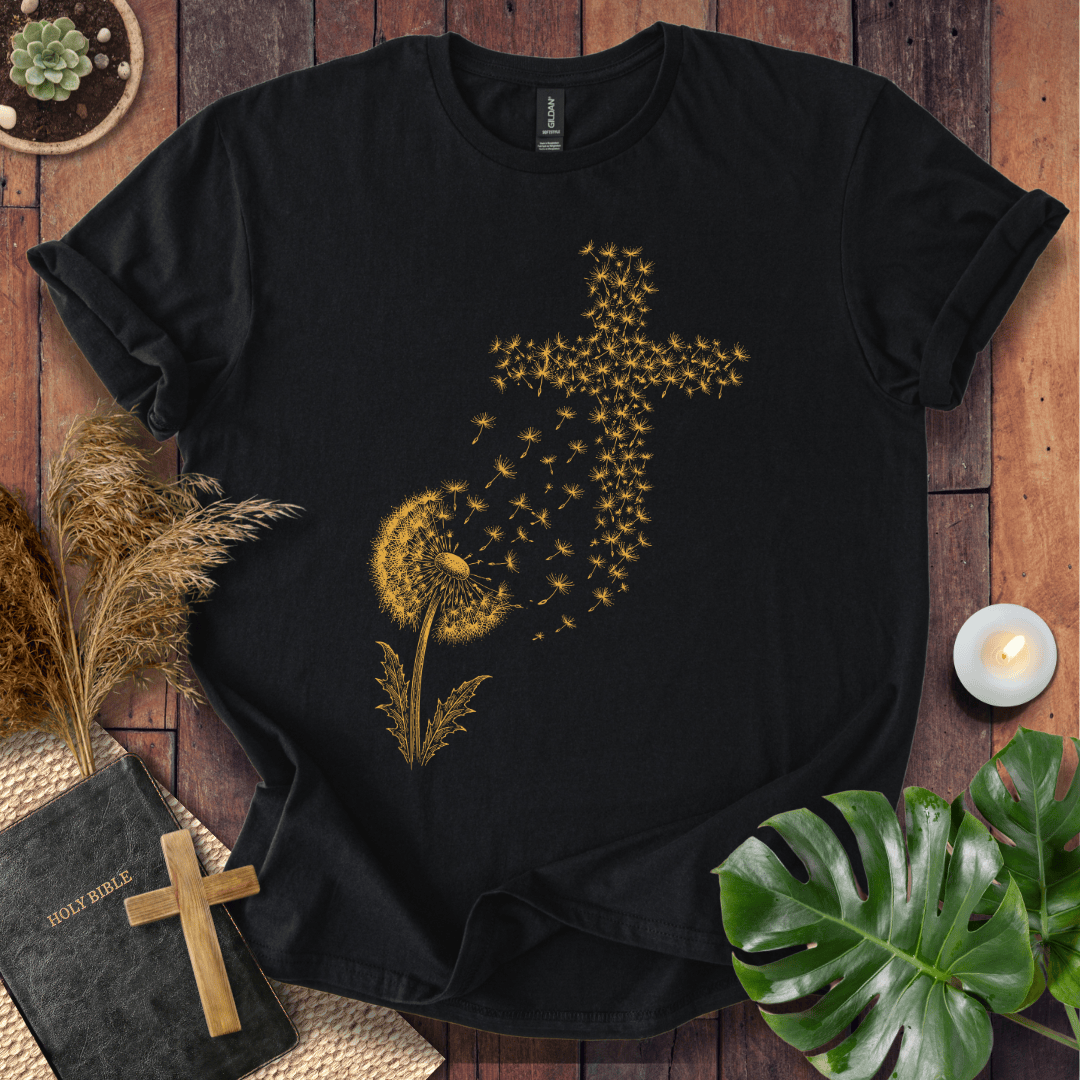 graphic t-shirt featuring a golden dandelion with seeds blowing in the wind to form a Christian cross shape.