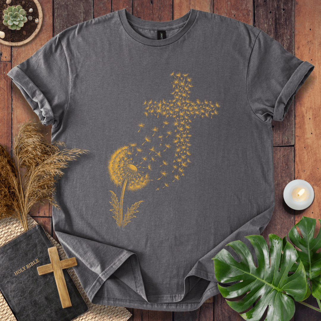 graphic t-shirt featuring a golden dandelion with seeds blowing in the wind to form a Christian cross shape.