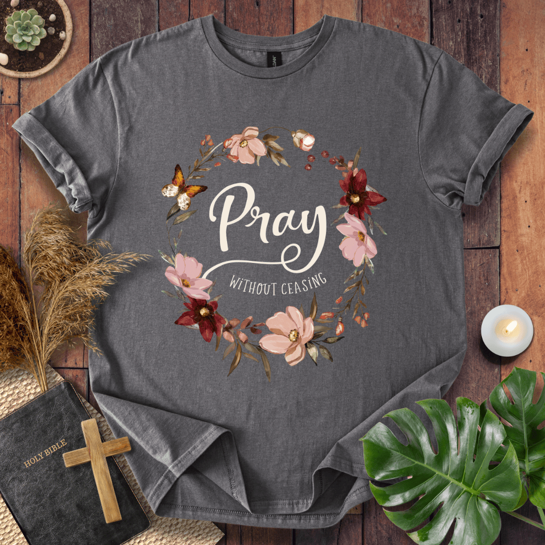 "Pray Without Ceasing" text inside a floral wreath with a butterfly on a shirt next to a Bible and cross.