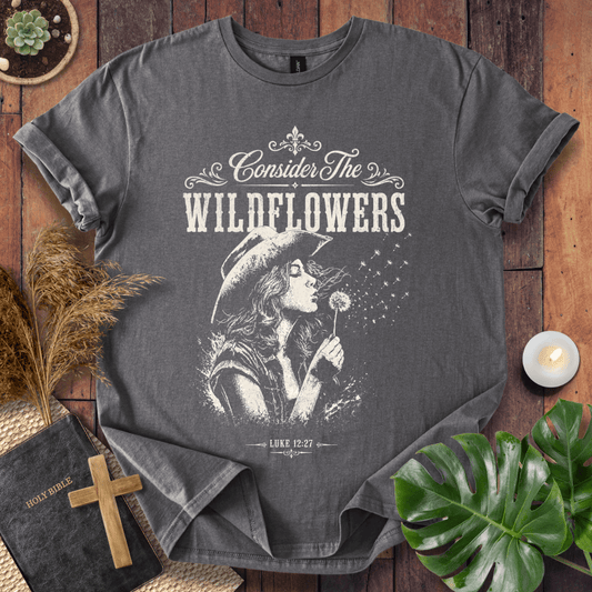 graphic tee reading Consider the Wildflowers Luke 12:27, featuring a woman in a cowboy hat blowing a dandelion.