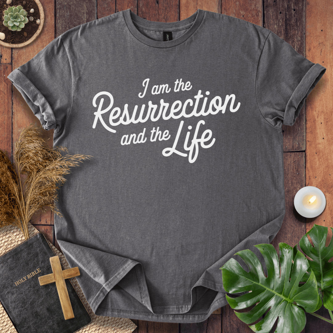 Christian t shirt for women featuring white script 'I am the Resurrection and the Life' on a rustic wood table.