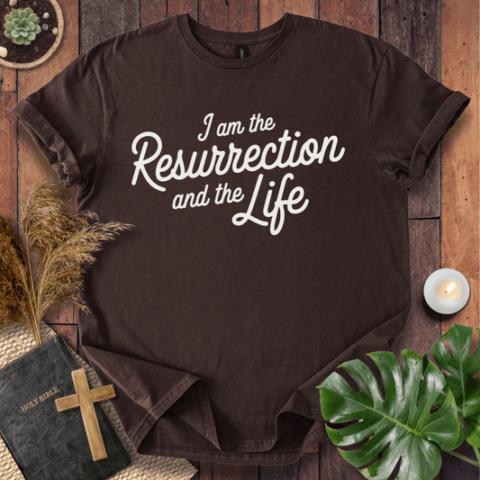 Christian t shirt for women featuring white script 'I am the Resurrection and the Life' on a rustic wood table.