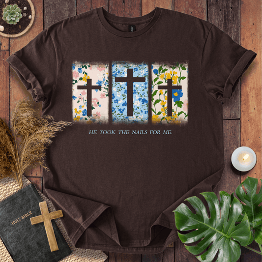 Christian Easter t-shirt with three floral crosses and "He Took The Nails For Me" text, styled on a rustic wood background.