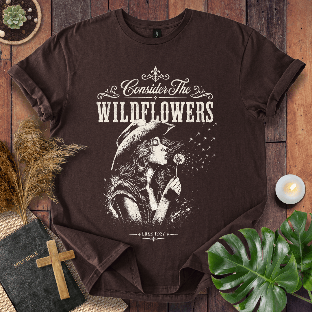 graphic tee reading Consider the Wildflowers Luke 12:27, featuring a woman in a cowboy hat blowing a dandelion.