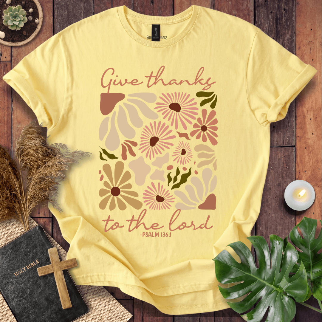 Give Thanks to the Lord Psalm 136:1 white graphic t-shirt with retro boho rust and sage wildflowers on a wood background.