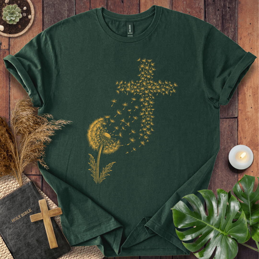 graphic t-shirt featuring a golden dandelion with seeds blowing in the wind to form a Christian cross shape.