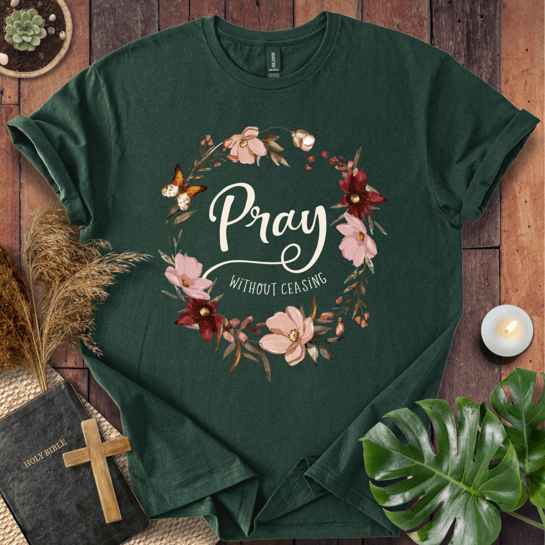 "Pray Without Ceasing" text inside a floral wreath with a butterfly on a shirt next to a Bible and cross.