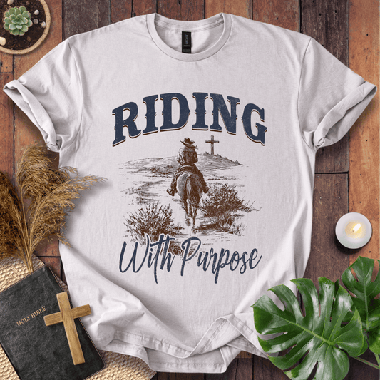 A lone rider on a horse approaching a cross on a Christian themed shirt with Riding With Purpose text.