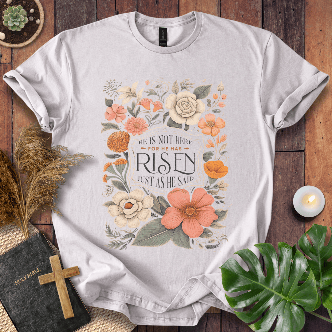 Christian Easter t-shirt with vintage flowers and He Is Risen Matthew 28:6 text on a rustic wood background.