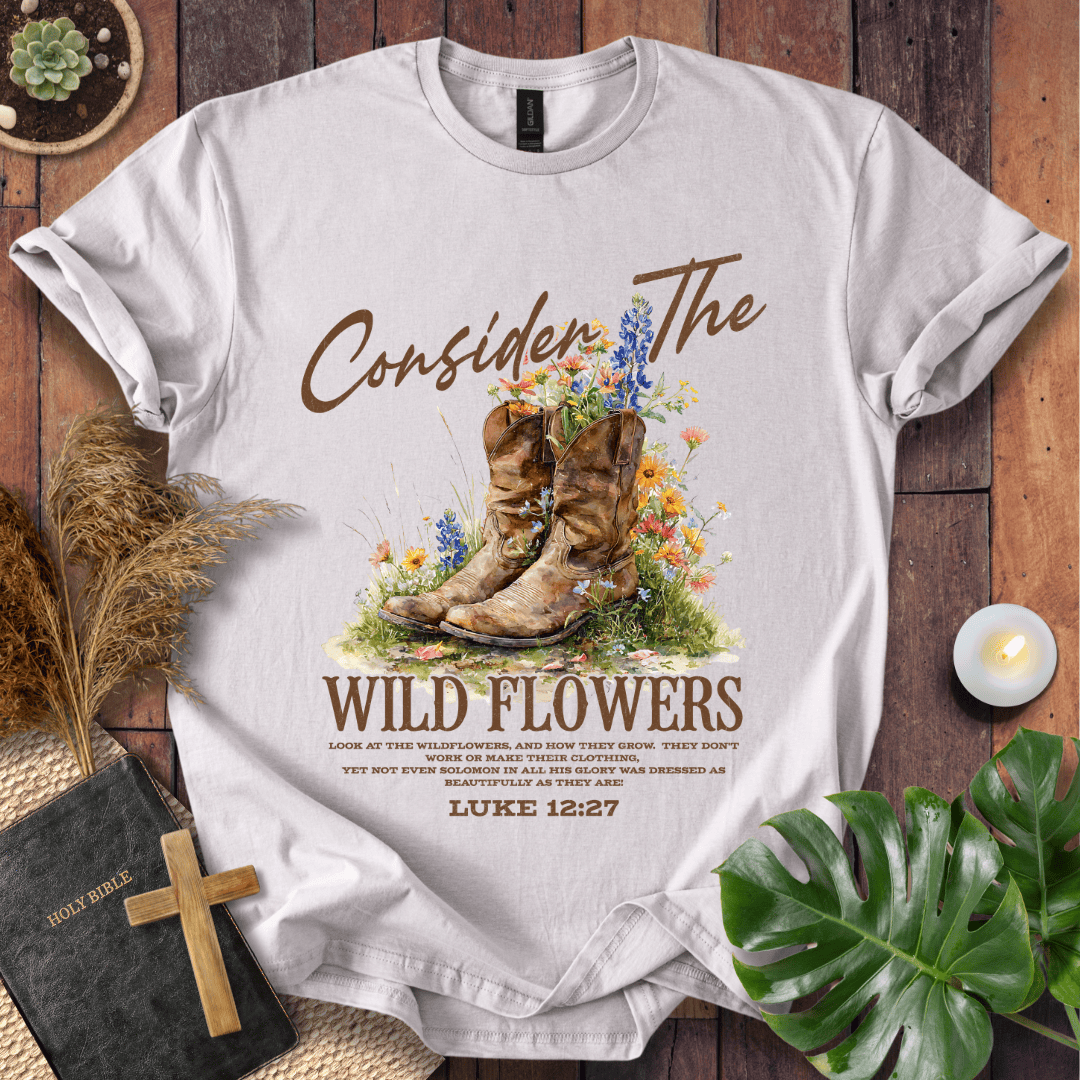 Western wildflower graphic tee with bible verse shirts text showing Luke 12:27 and boots on a natural cream shirt.