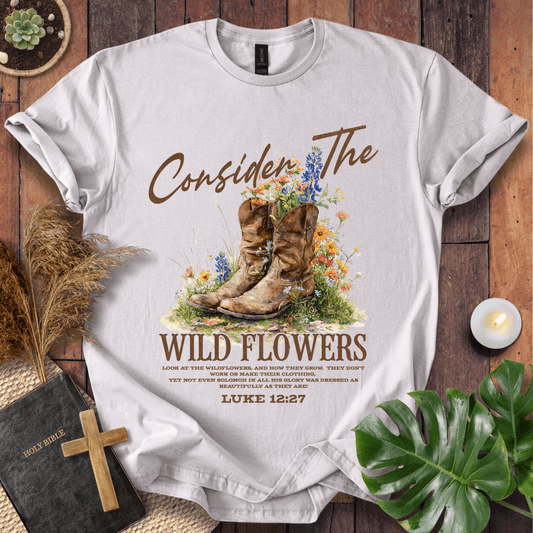 Western wildflower graphic tee with bible verse shirts text showing Luke 12:27 and boots on a natural cream shirt.
