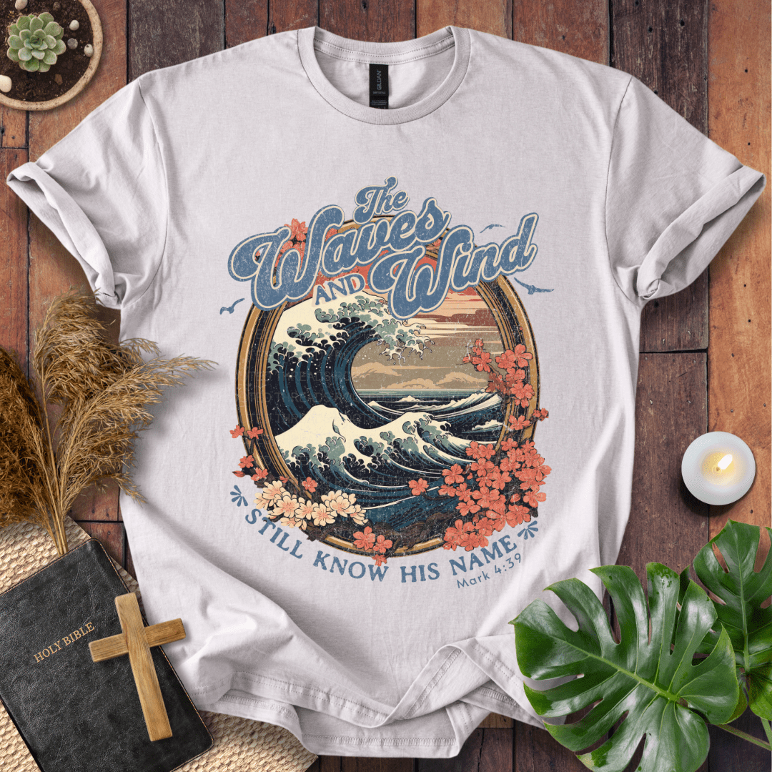 The Waves and Wind Still Know His Name Christian t-shirt in sand—vintage wave, sunset, and floral frame, Mark 4:39.