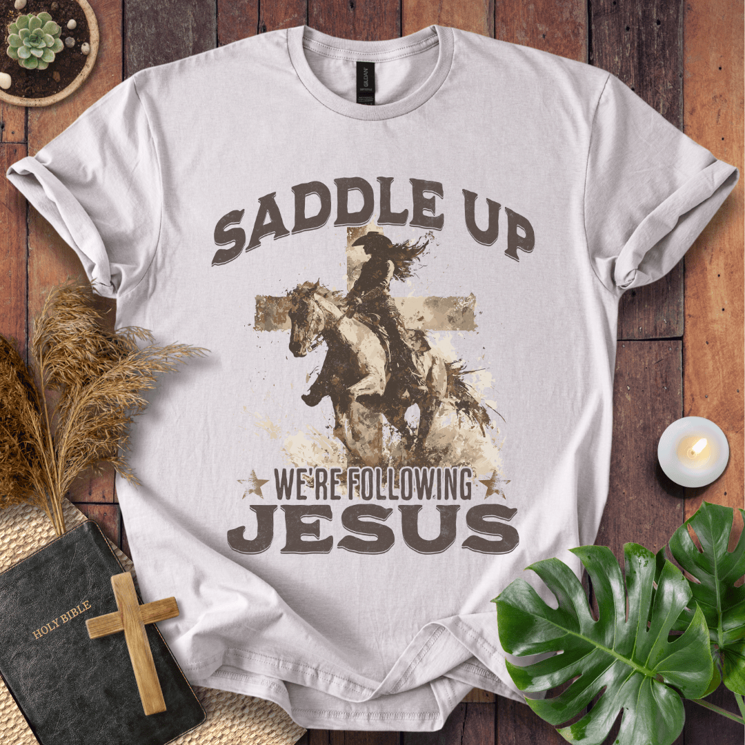 t-shirt featuring a cowgirl riding a horse in front of a cross with the text Saddle Up We're Following Jesus.