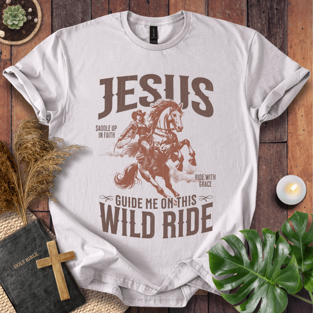 White t-shirt with 'Jesus Guide Me on This Wild Ride' graphic on a wooden surface with decor items.