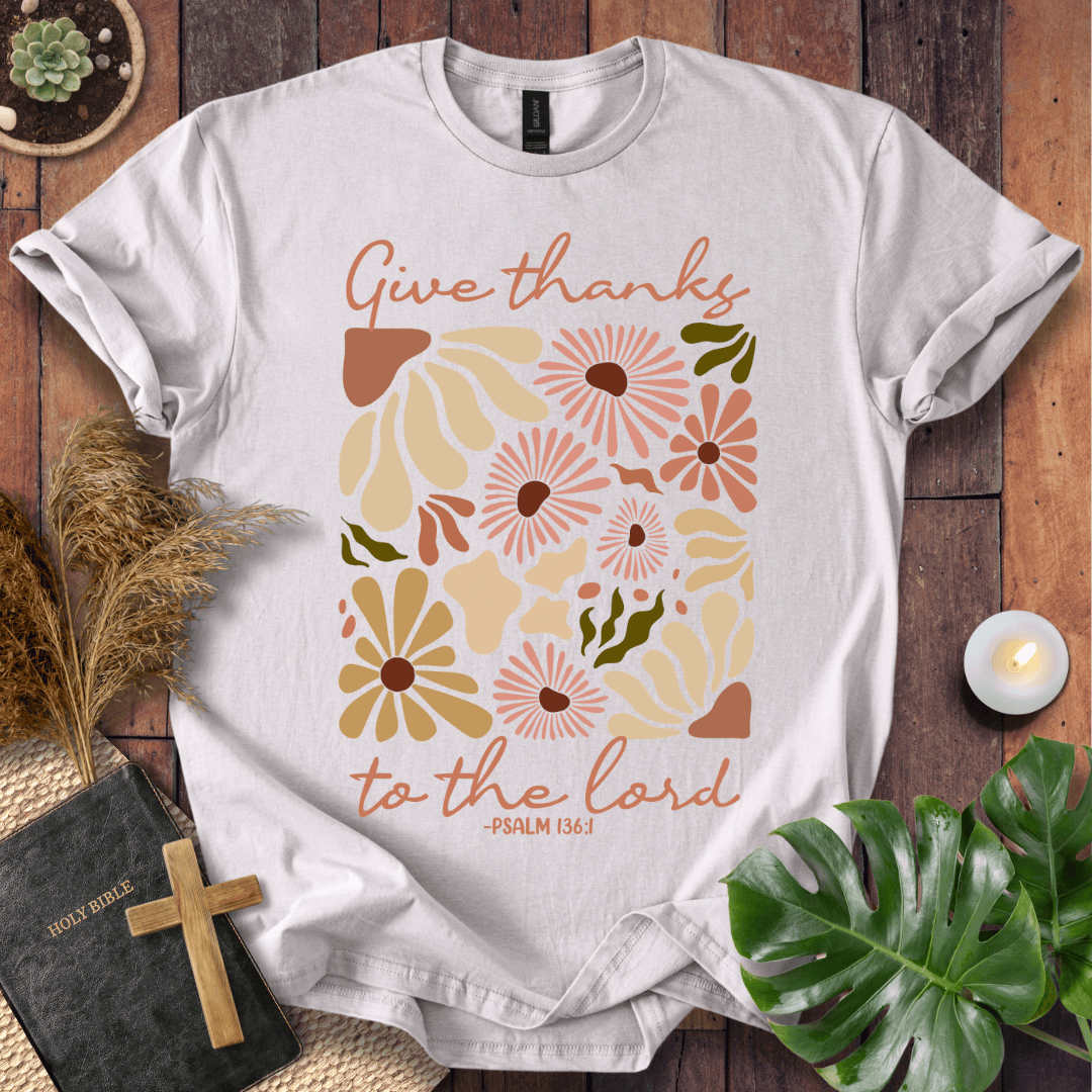 Give Thanks to the Lord Psalm 136:1 white graphic t-shirt with retro boho rust and sage wildflowers on a wood background.