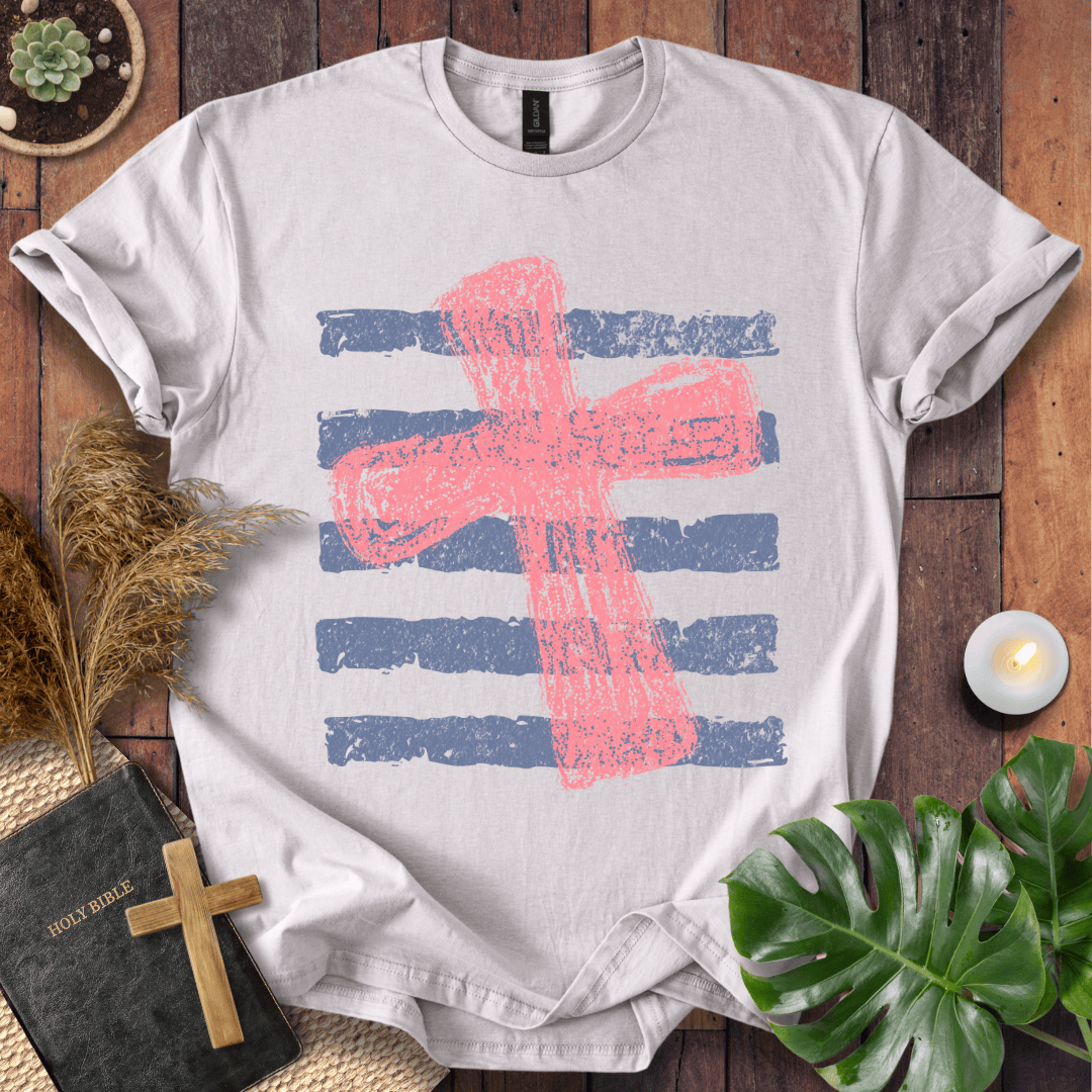 Distressed pink cross over blue horizontal stripes on a t-shirt, styled with a Bible and wooden cross.