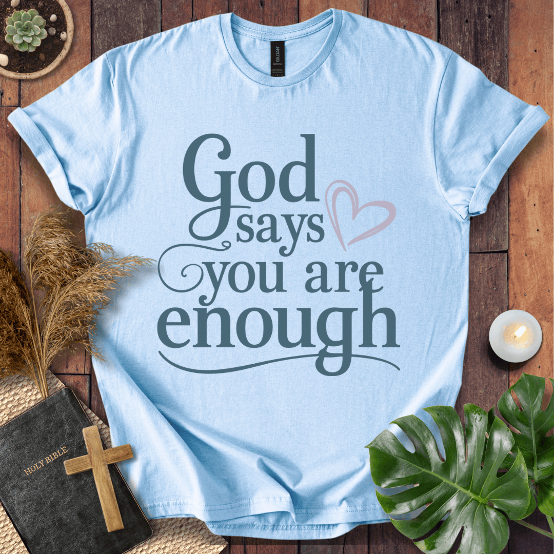 "God says you are enough" printed in teal on a sand Christian t-shirt for women, styled with a Bible and wooden cross.