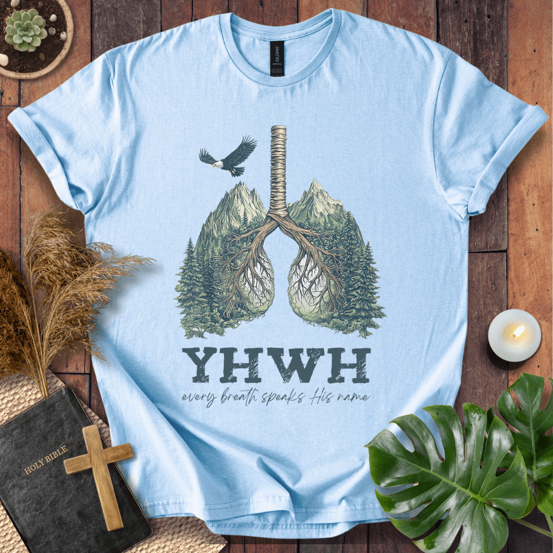 Christian t-shirt with YHWH design, tree-lung illustration, mountains, and “Every Breath Speaks His Name” text, laid flat with Bible and plants.