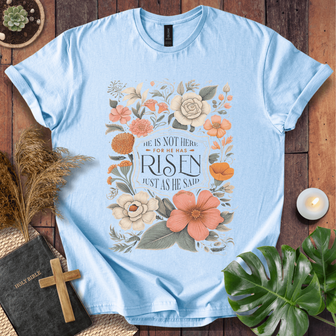 Christian Easter t-shirt with vintage flowers and He Is Risen Matthew 28:6 text on a rustic wood background.