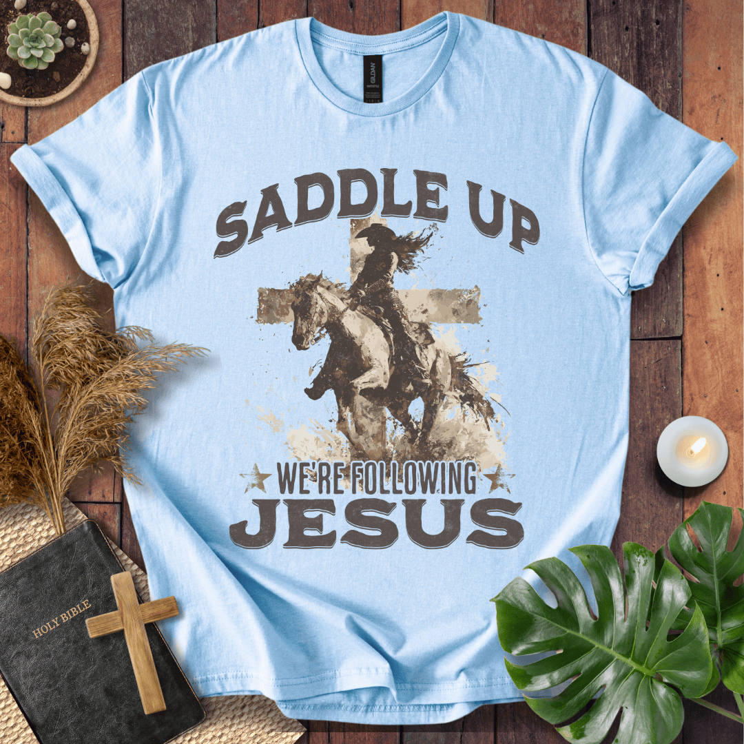 t-shirt featuring a cowgirl riding a horse in front of a cross with the text Saddle Up We're Following Jesus.