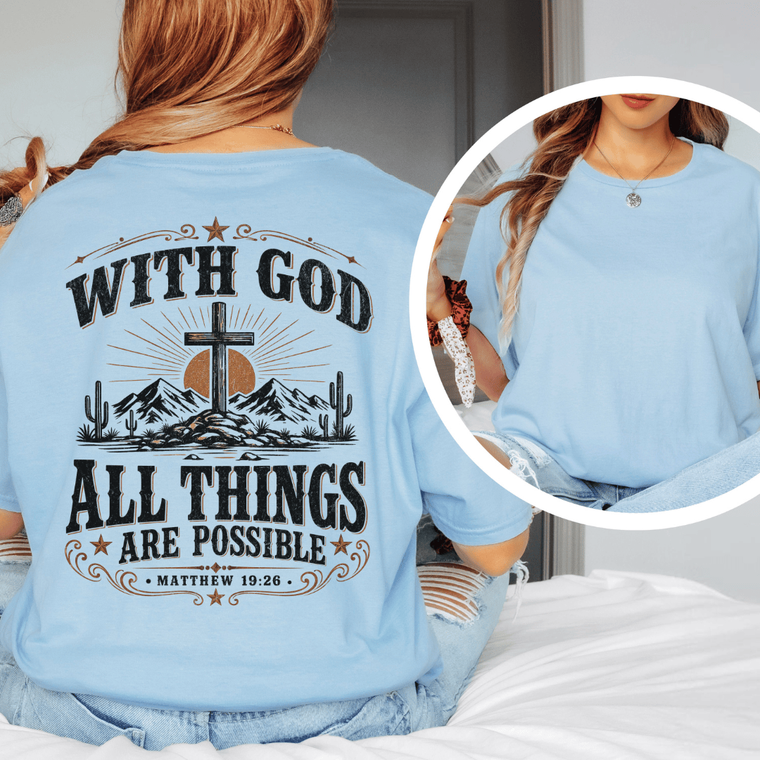 A woman sitting on a bed wearing a western faith shirt featuring a desert cross design and Matthew 19:26 scripture.