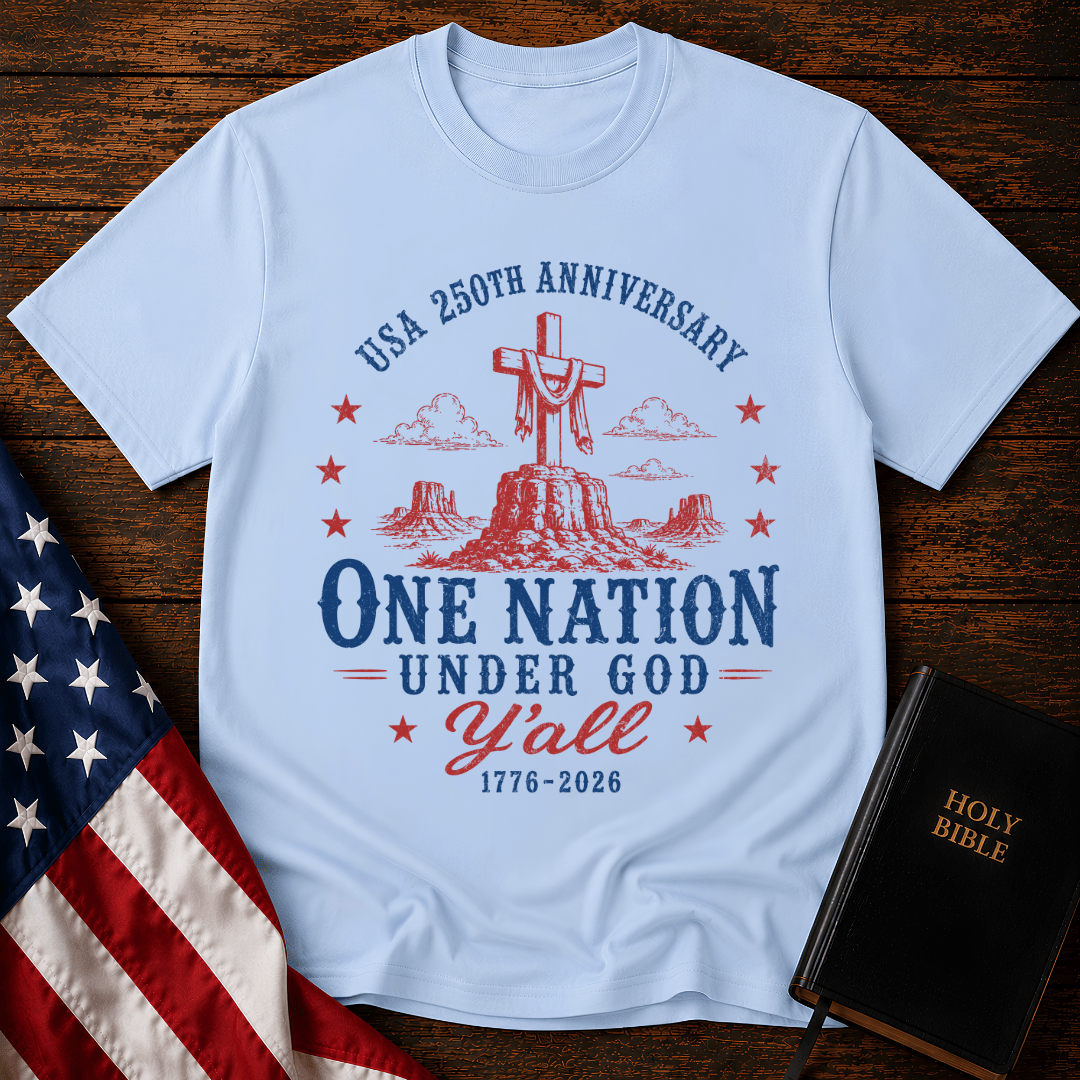 Patriotic western graphic tee featuring a wooden cross on a desert mesa with text One Nation Under God Y'all 1776-2026.