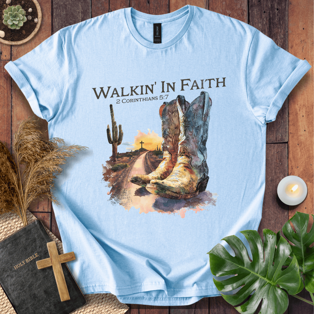 Light blue t-shirt with cowboy boots and desert scene design on a wooden surface.