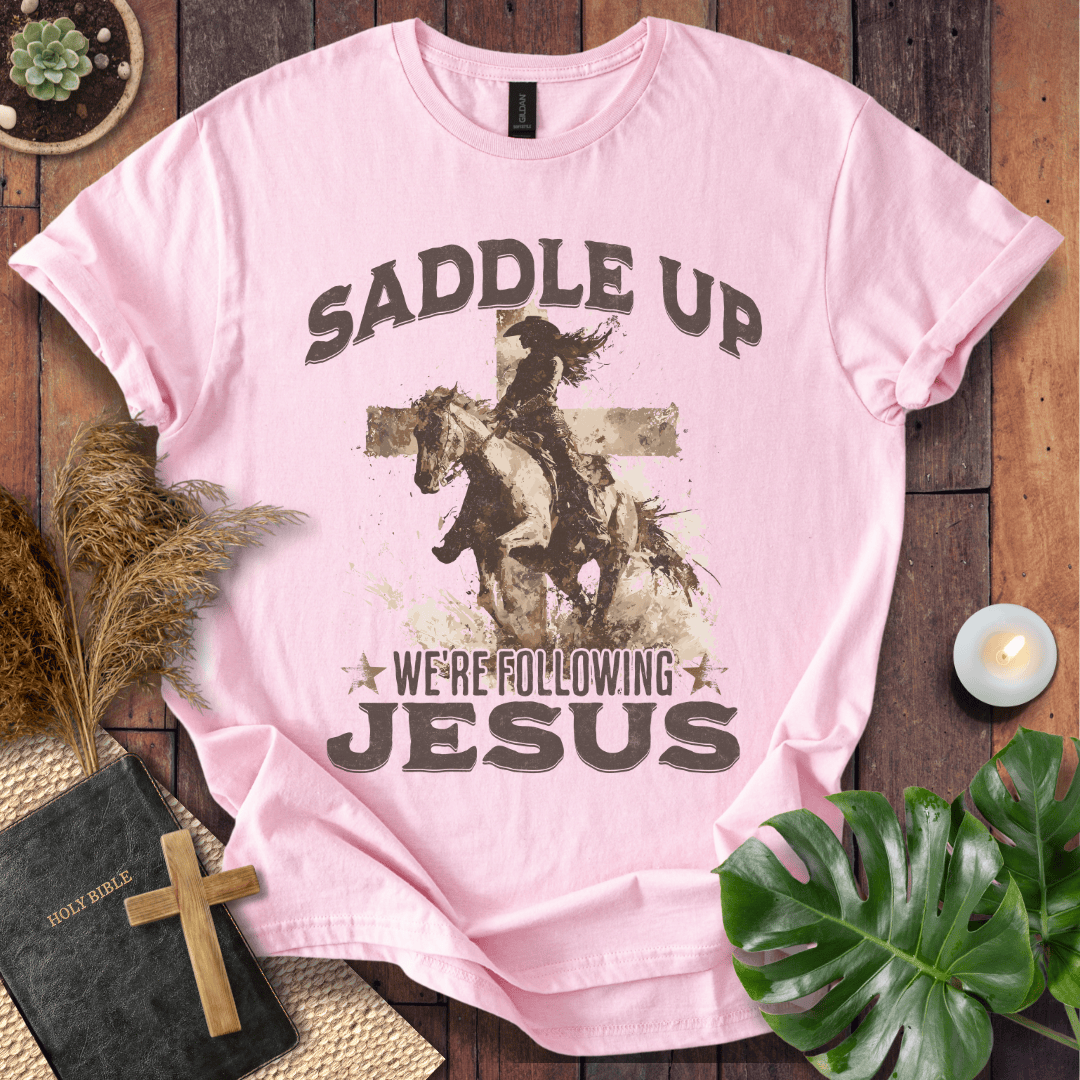 t-shirt featuring a cowgirl riding a horse in front of a cross with the text Saddle Up We're Following Jesus.