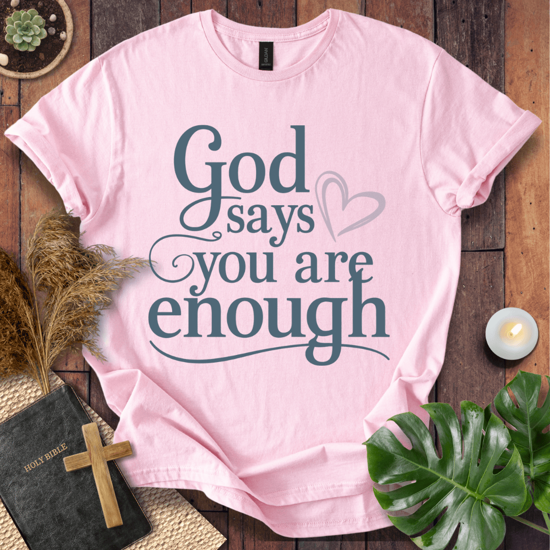 "God says you are enough" printed in teal on Christian t-shirt for women, styled with a Bible and wooden cross.