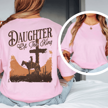 A woman wearing a graphic t-shirt with a western desert cross, cowboy on a horse, and Daughter of the King text.