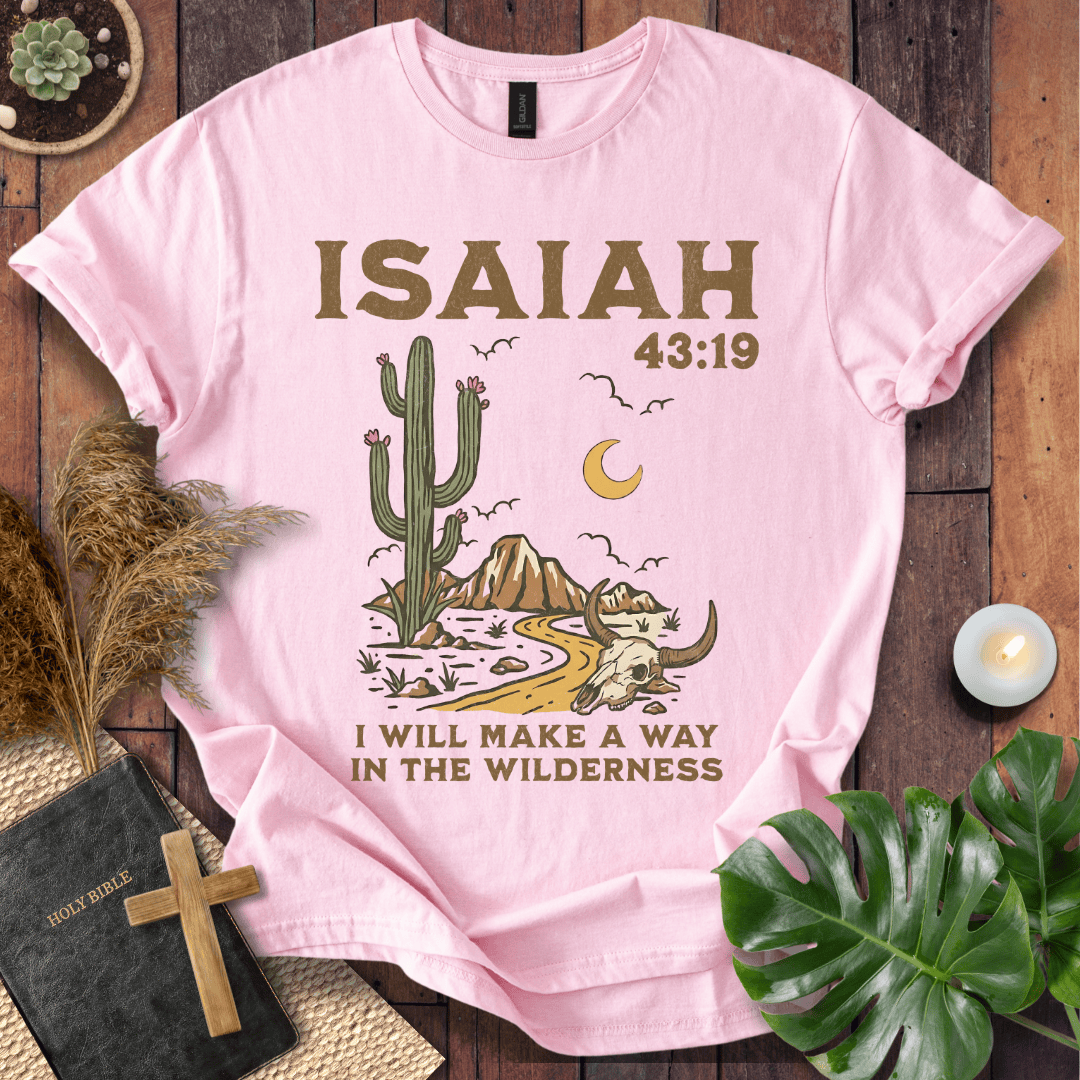 Pink t-shirt with cactus and Bible verse design on a wooden surface with plants and a cross.