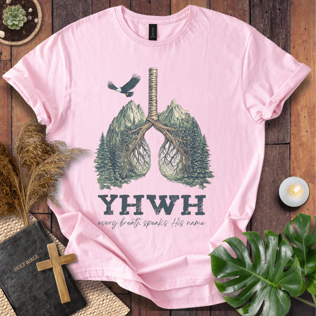 Christian t-shirt with YHWH design, tree-lung illustration, mountains, and “Every Breath Speaks His Name” text, laid flat with Bible and plants.