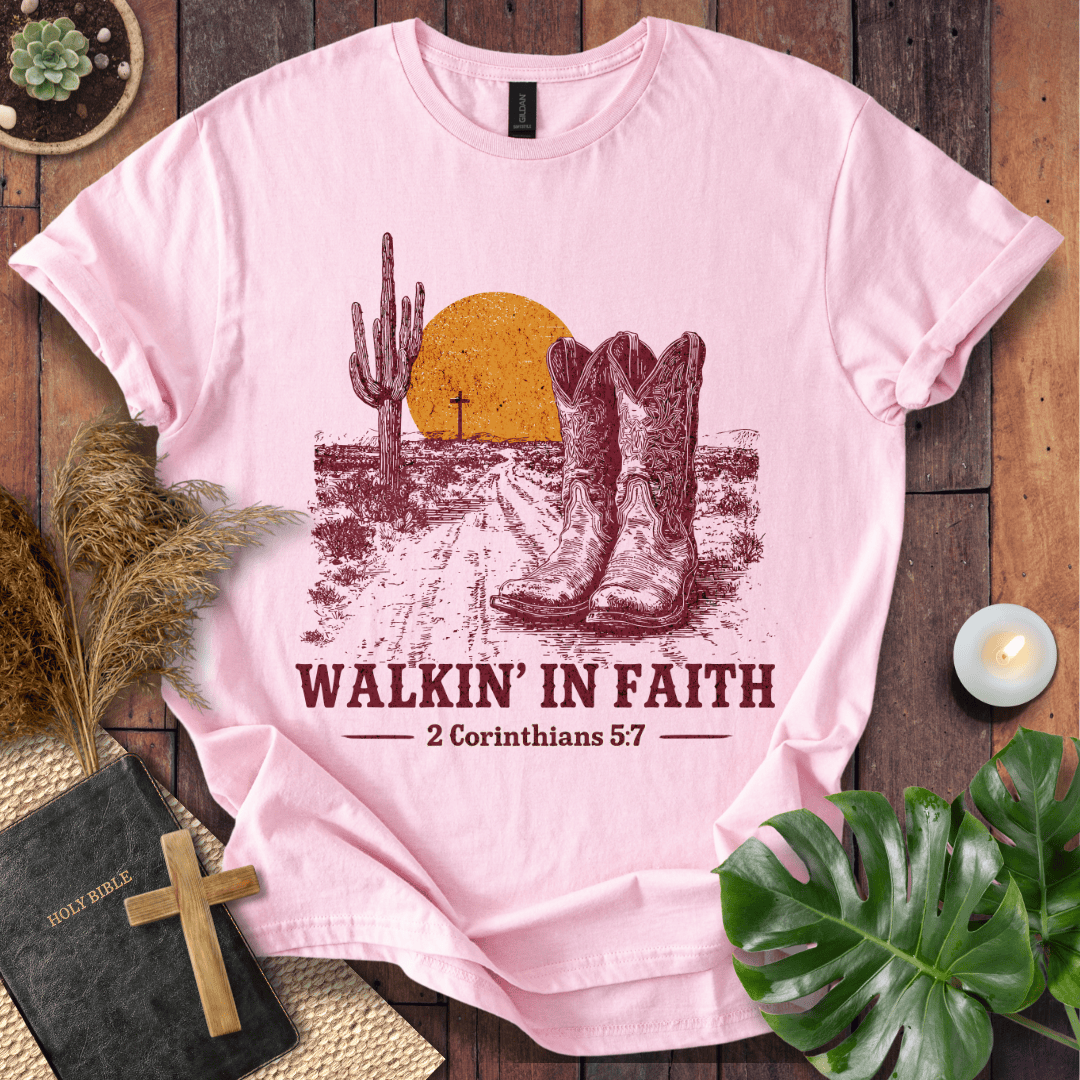 Pink t-shirt with desert graphic and 'Walkin' in Faith' text on a wooden surface.
