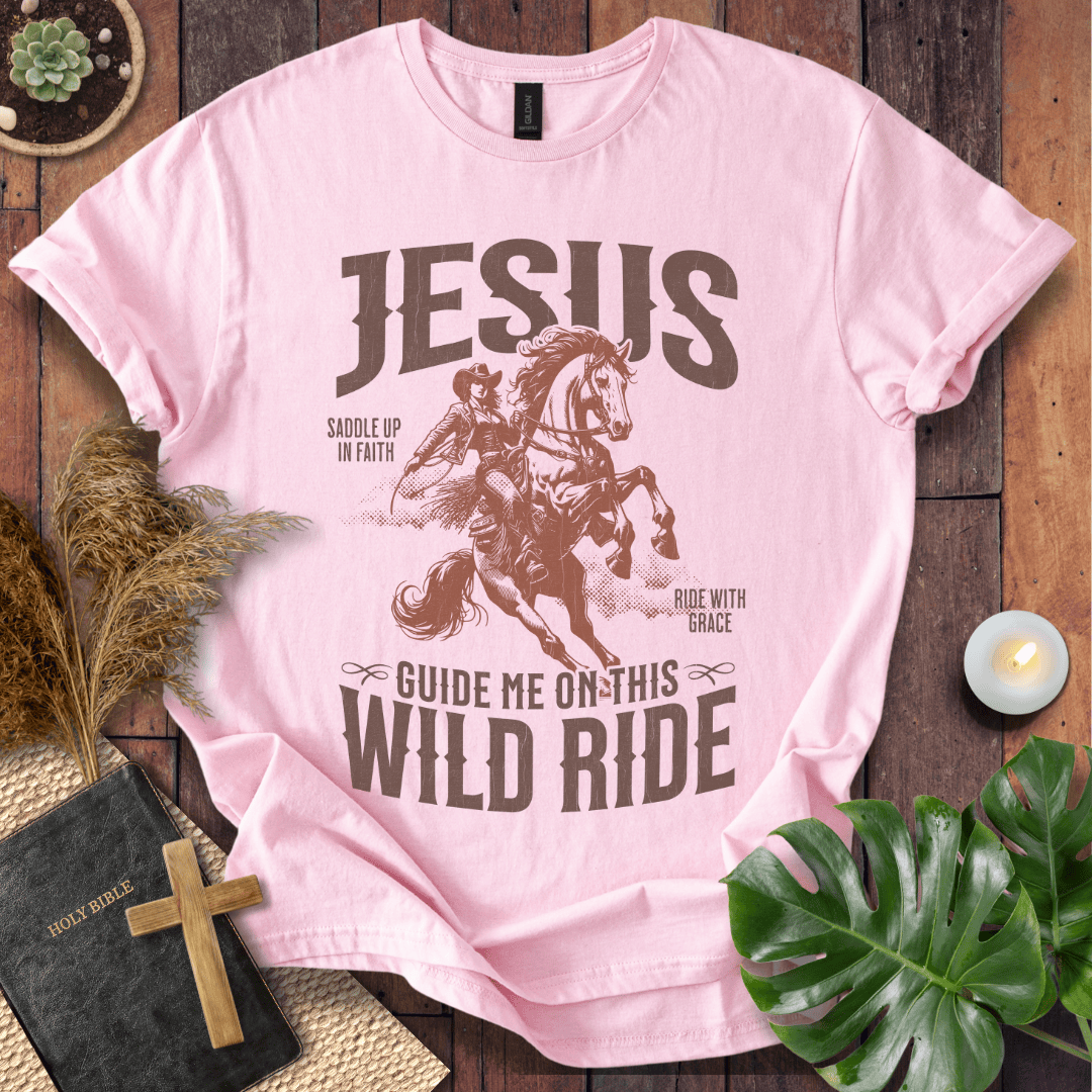 Pink t-shirt with 'Jesus' graphic and text on a wooden surface with decor items.