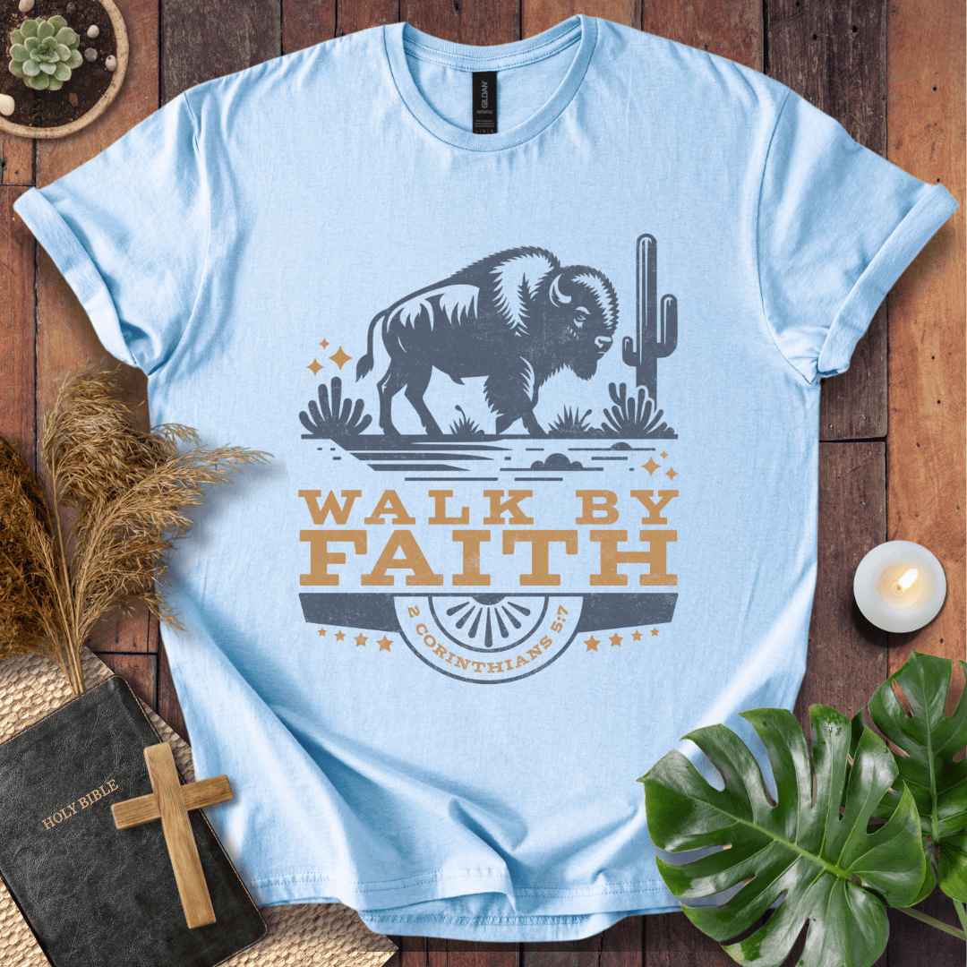 Light blue t-shirt with a graphic of a bison and cactus, and 'Walk by Faith' text on a wooden surface.