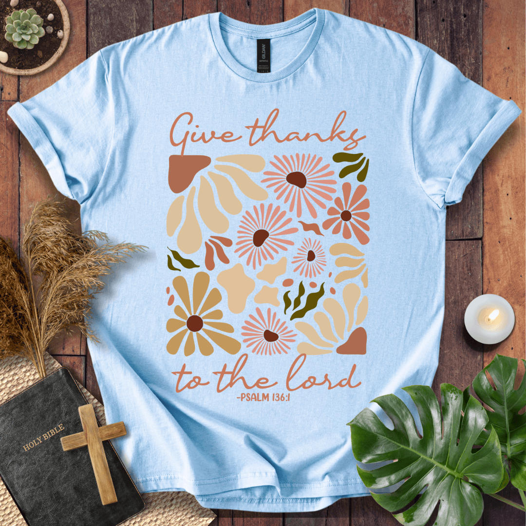 Give Thanks to the Lord Psalm 136:1 white graphic t-shirt with retro boho rust and sage wildflowers on a wood background.