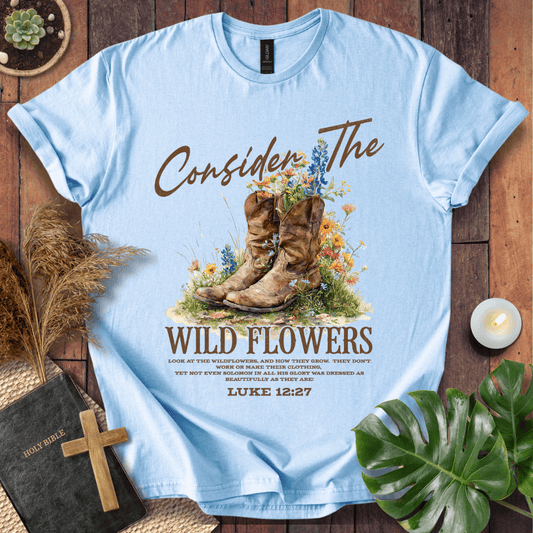 Western wildflower graphic tee with bible verse shirts text showing Luke 12:27 and boots on a natural cream shirt.