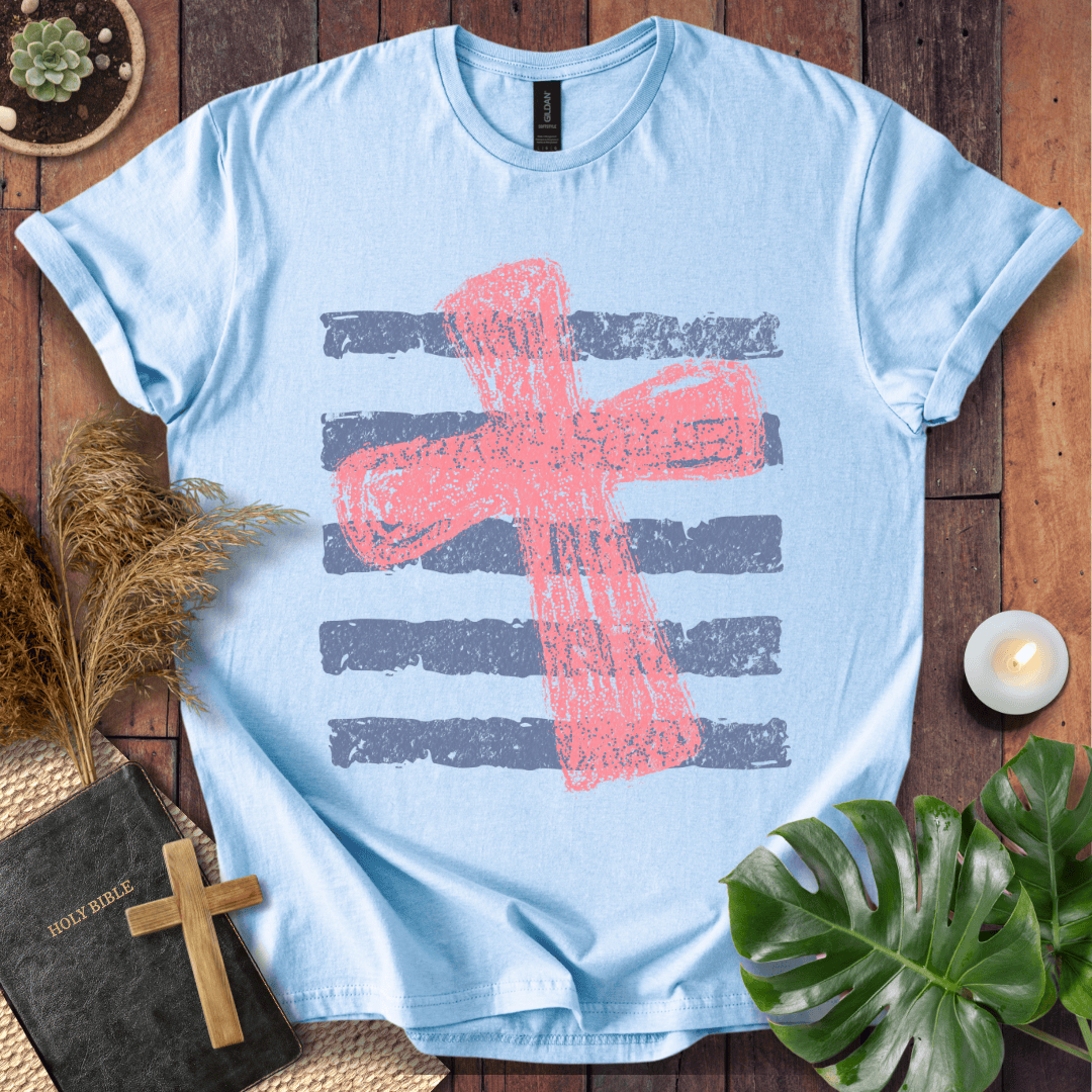 Distressed pink cross over blue horizontal stripes on a t-shirt, styled with a Bible and wooden cross.